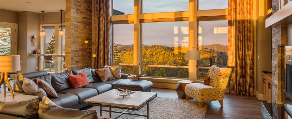 Modernes Wohnzimmer mit Panoramafenster und Blick auf Waldlandschaft bei Sonnenuntergang